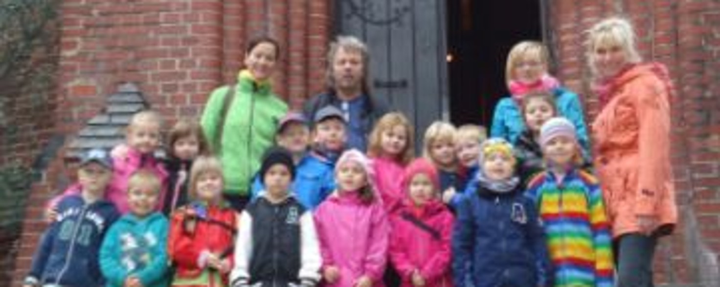 Eine Gruppe Kinder mit ihren Erzieherinnen steht vor einer großen Tür eines Backstein-Gebäudes