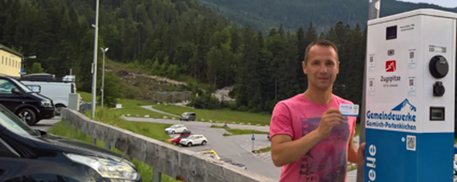 Ein Mann steht mit einer Ladekarte an einer E-Auto-Ladestation am Fuße der Zugspitze