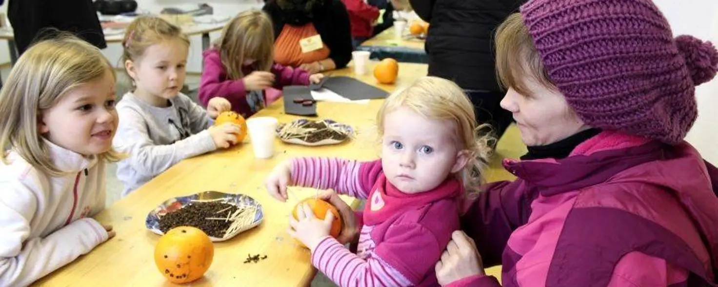 Mehrere Kinder sitzen an einem Tisch und stecken Nelken in Orangen