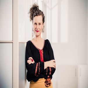 Frau mit lockigen Haaren lächelt und trägt eine schwarz-rote Bluse.