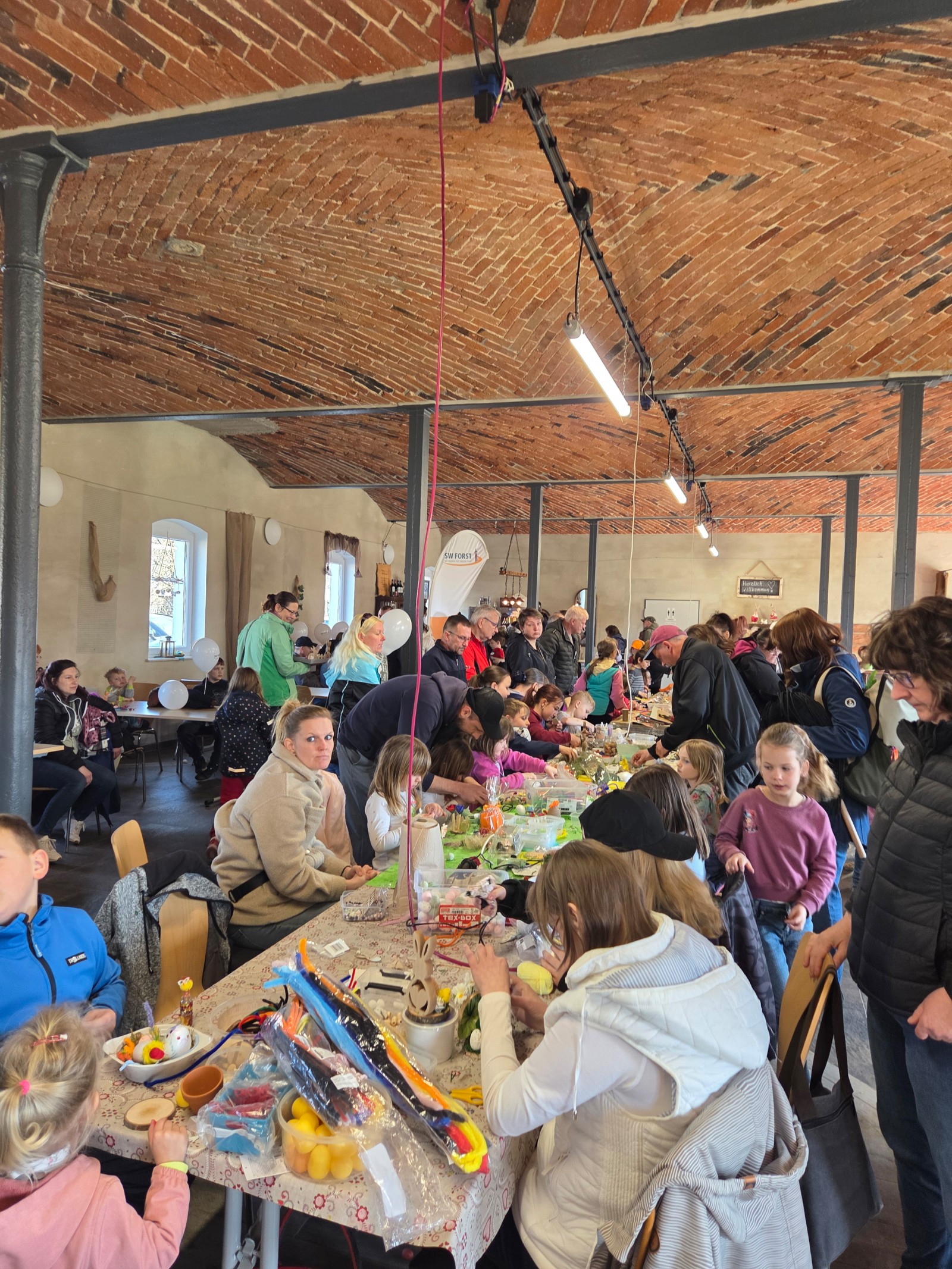 An einem großen Tisch sitzen Kinder und Eltern und basteln für Ostern