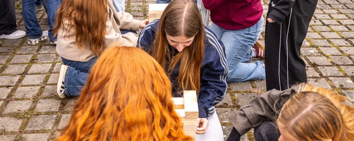 Auf dem Boden sind ein paar junge Mädchen in der Hocke und bauen einen Turm aus Holzklötzen.