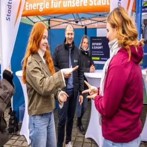 Zwei junge Mädchen spielen vor dem orangefarbigen Pavillion der Stadtwerke Forst Schere, Stein, Papier.