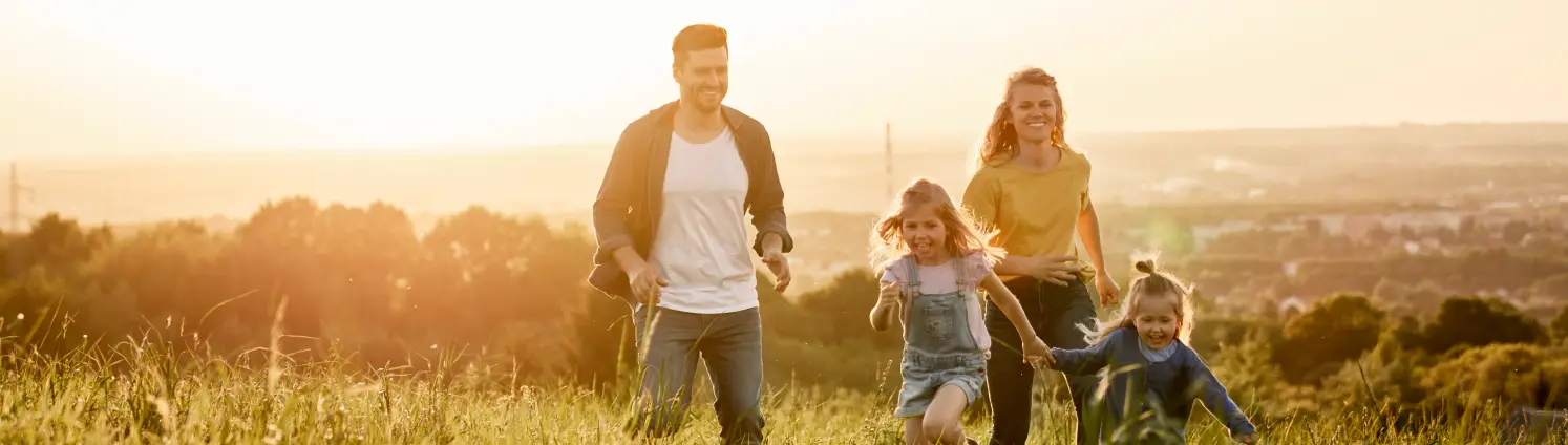 Familie läuft bei Sonnenuntergang über eine Wiese.