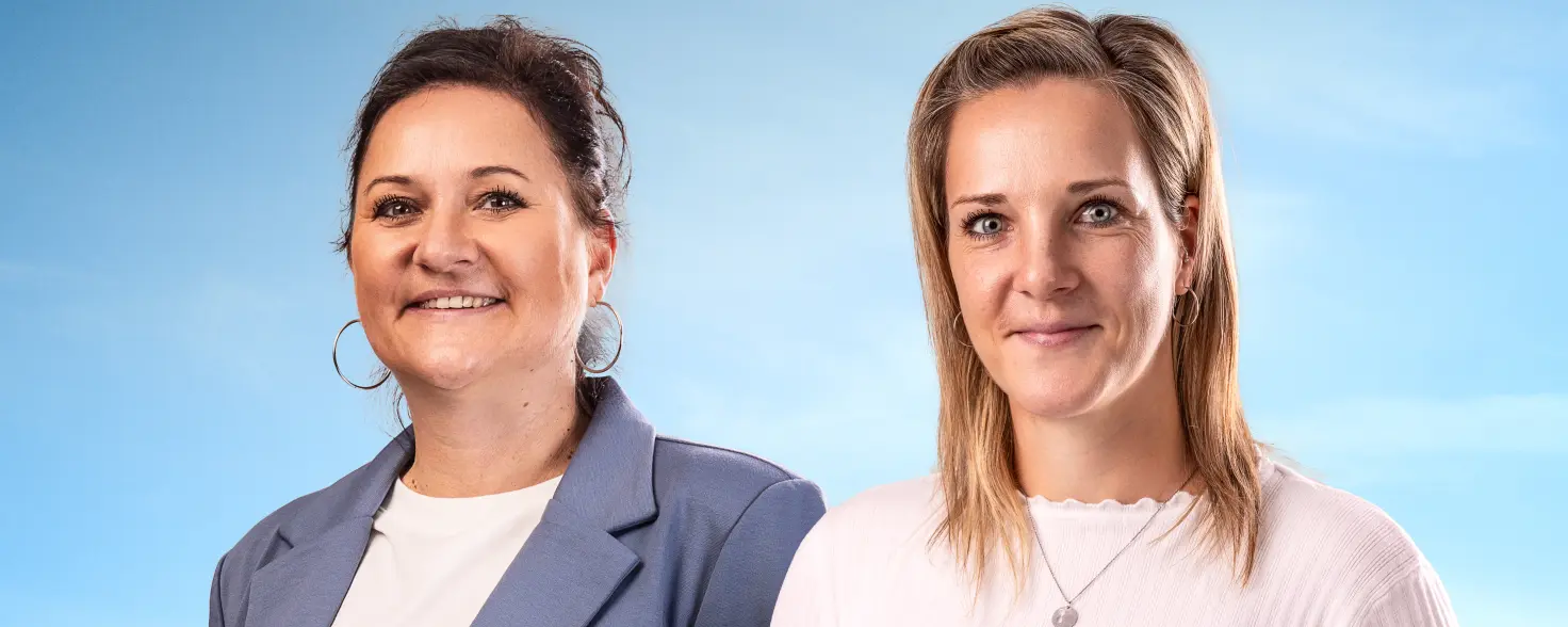 Drei Frauen in Business-Outfits stehen nebeneinander und lächeln in die Kamera